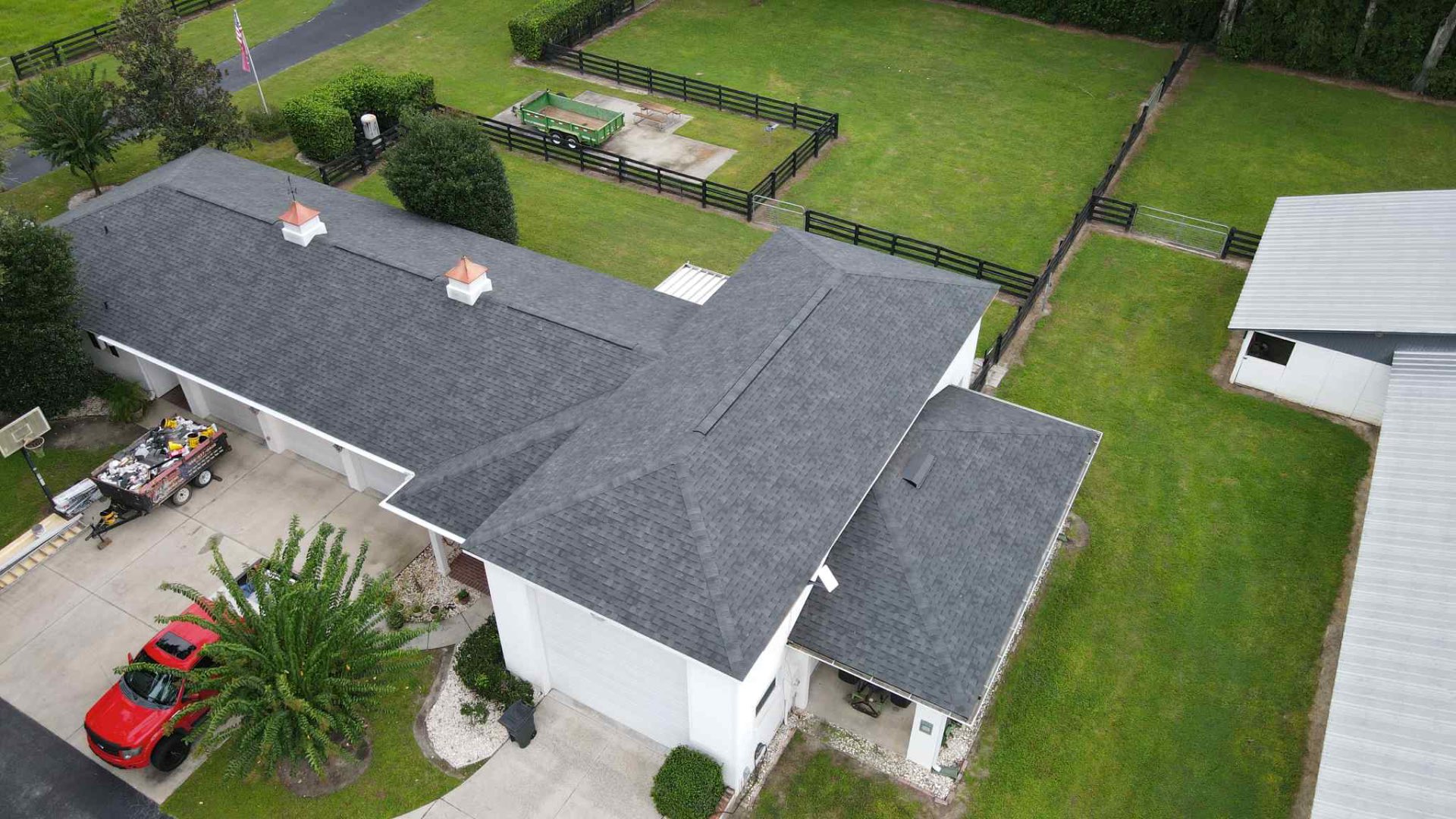 Aerial view of long ranch-style home with charcoal architectural shingle roof and copper cupolas