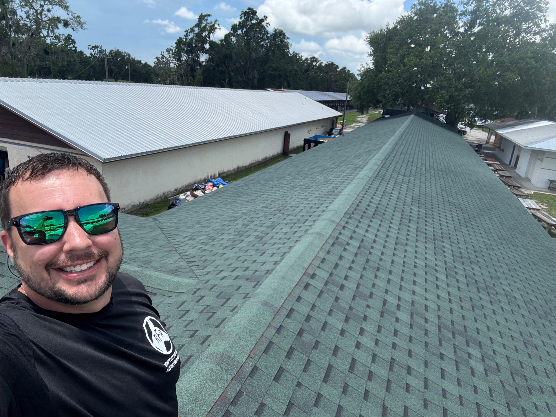 Raymond Frankart smiling on completed green shingle roof beside matching silver metal building